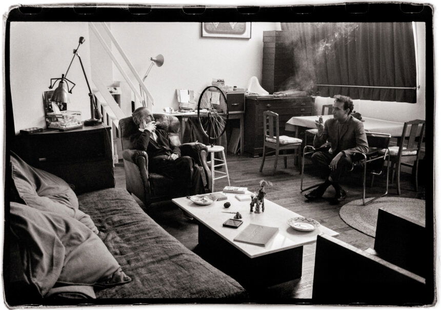 Black and white photo of artists Daniel Spoerri and Marcel Duchamp sitting together in conversation in Paris, early 1960s. Captured by Vera Mercer.