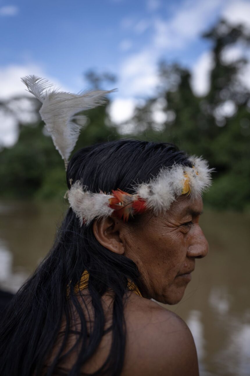 Waorani community members in traditional clothing made from natural fibers, with some younger individuals also wearing modern clothes, in the Amazon rainforest.