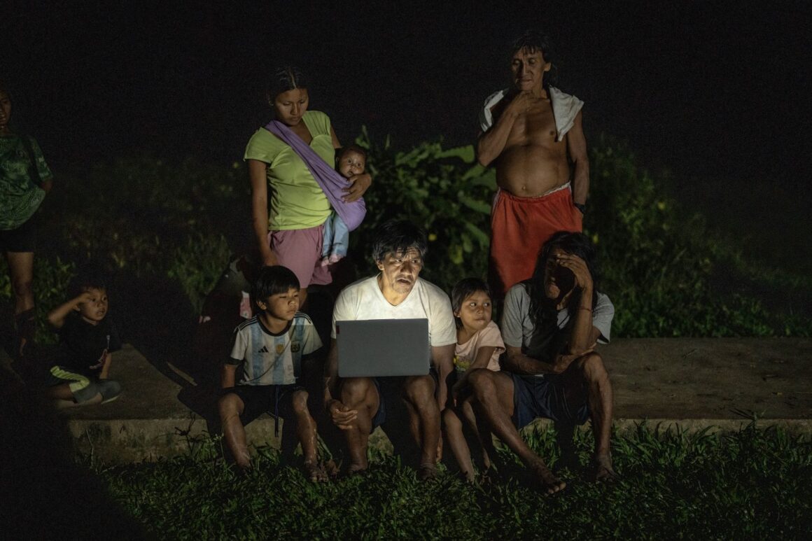 Missionaries showing videos on a laptop to a group of Waorani people in a community setting in the Amazon.
