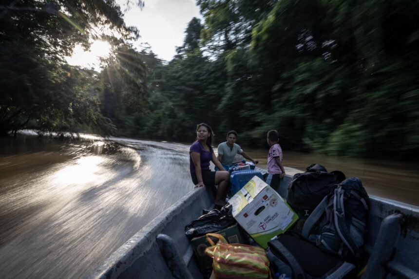 Ground-level view of the remote Bameno Waorani settlement, showing traditional dwellings nestled in the Amazon rainforest beside a river.