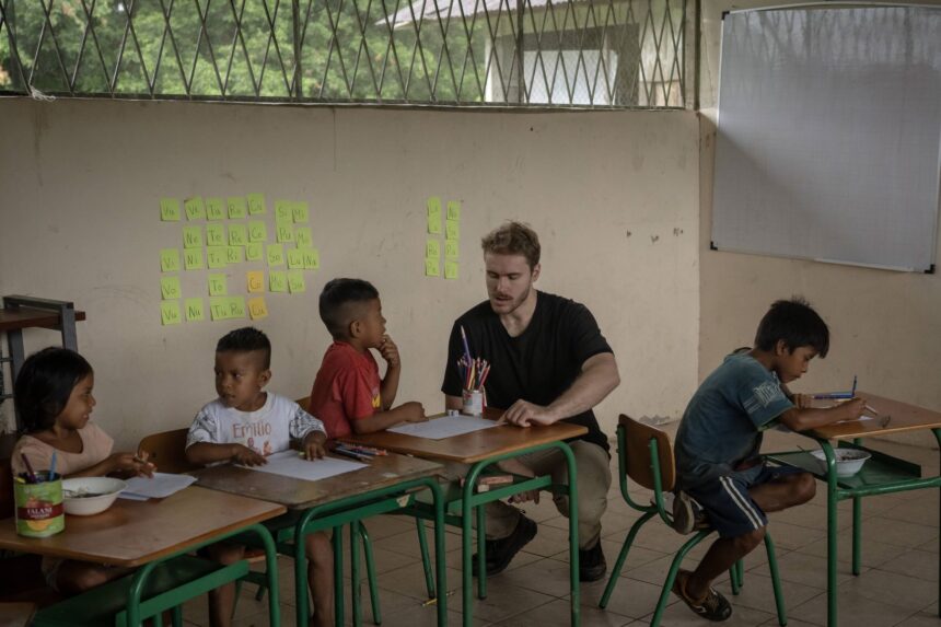 Waorani children and teachers inside a school building in the Amazon, with volunteers present.