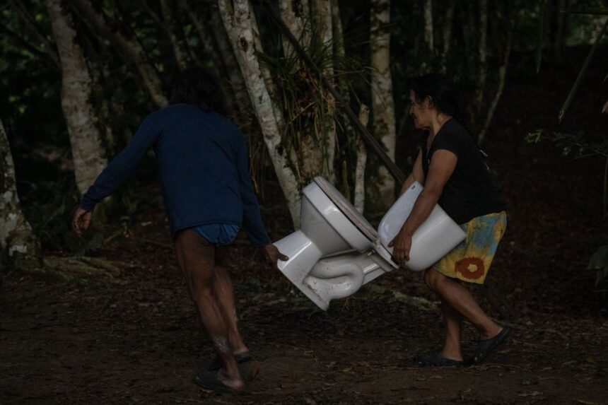 Waorani community members carrying a white toilet through the dense Amazon rainforest.