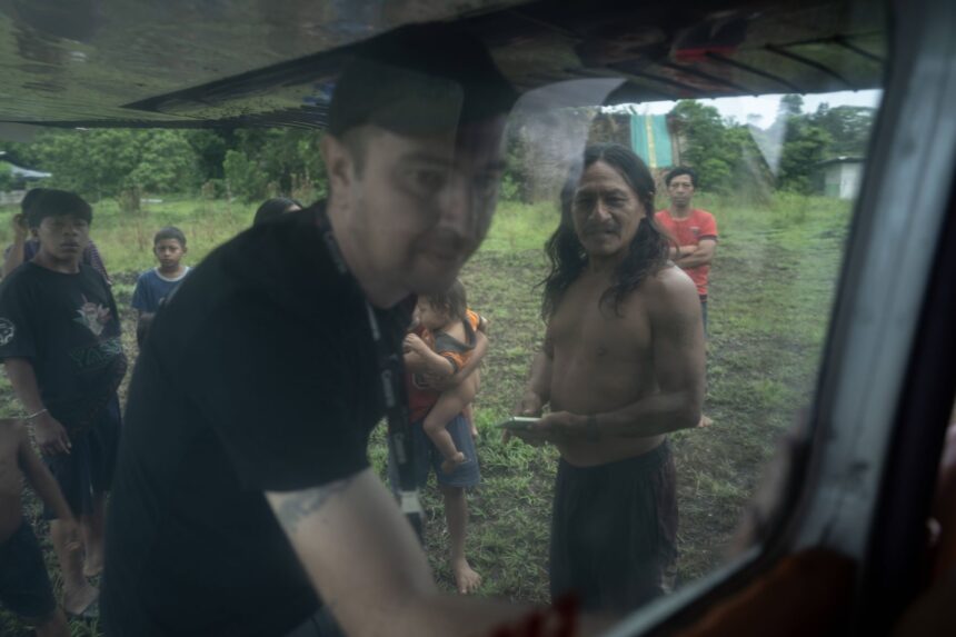 Waorani community members standing near a small aircraft on a dirt airstrip in the Amazon rainforest.