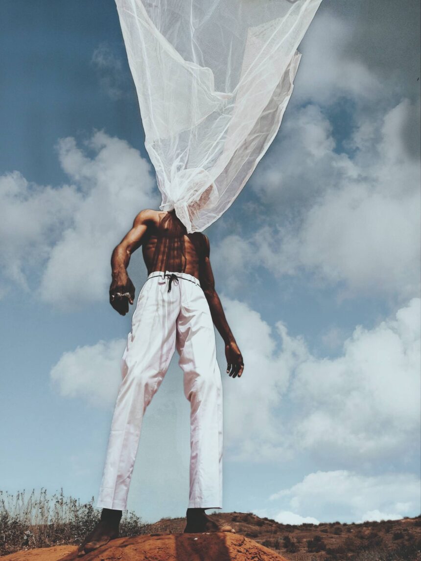 Shirtless man with white tulle on head against sky.
